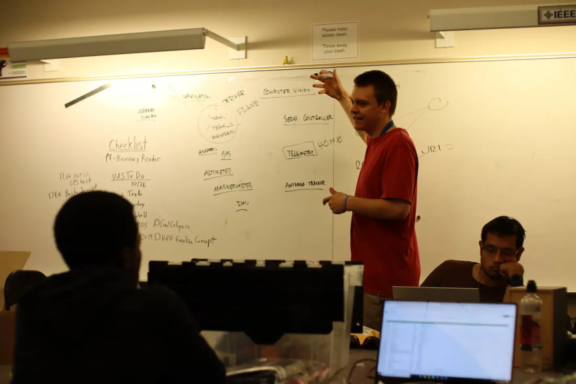 Aviatr member explaining concepts on a whiteboard to other members in a classroom